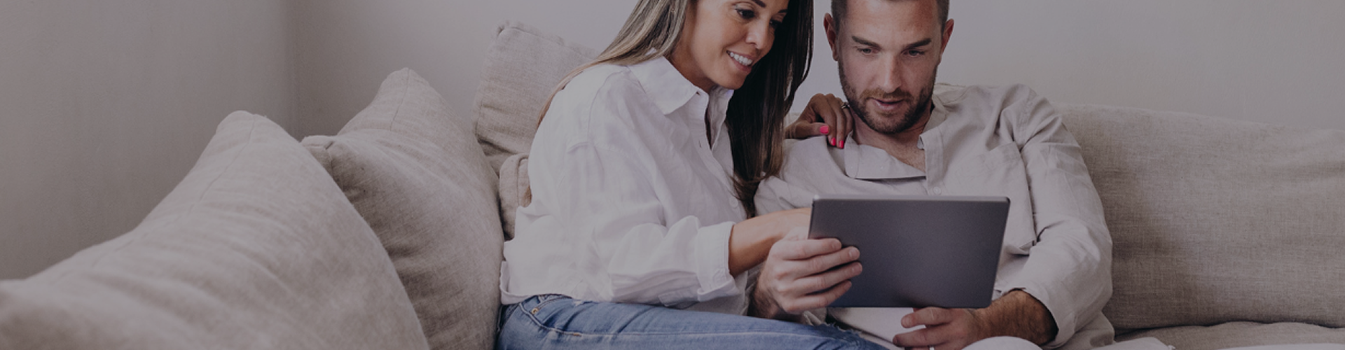 Couple sitting on the couch holding a tablet banner