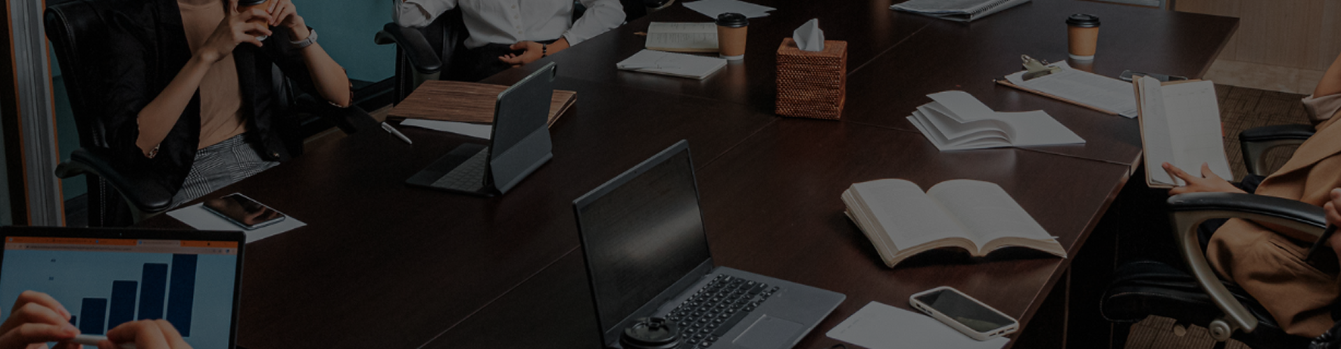 Team seated around a conference room table reading books, phones, and graphs banner